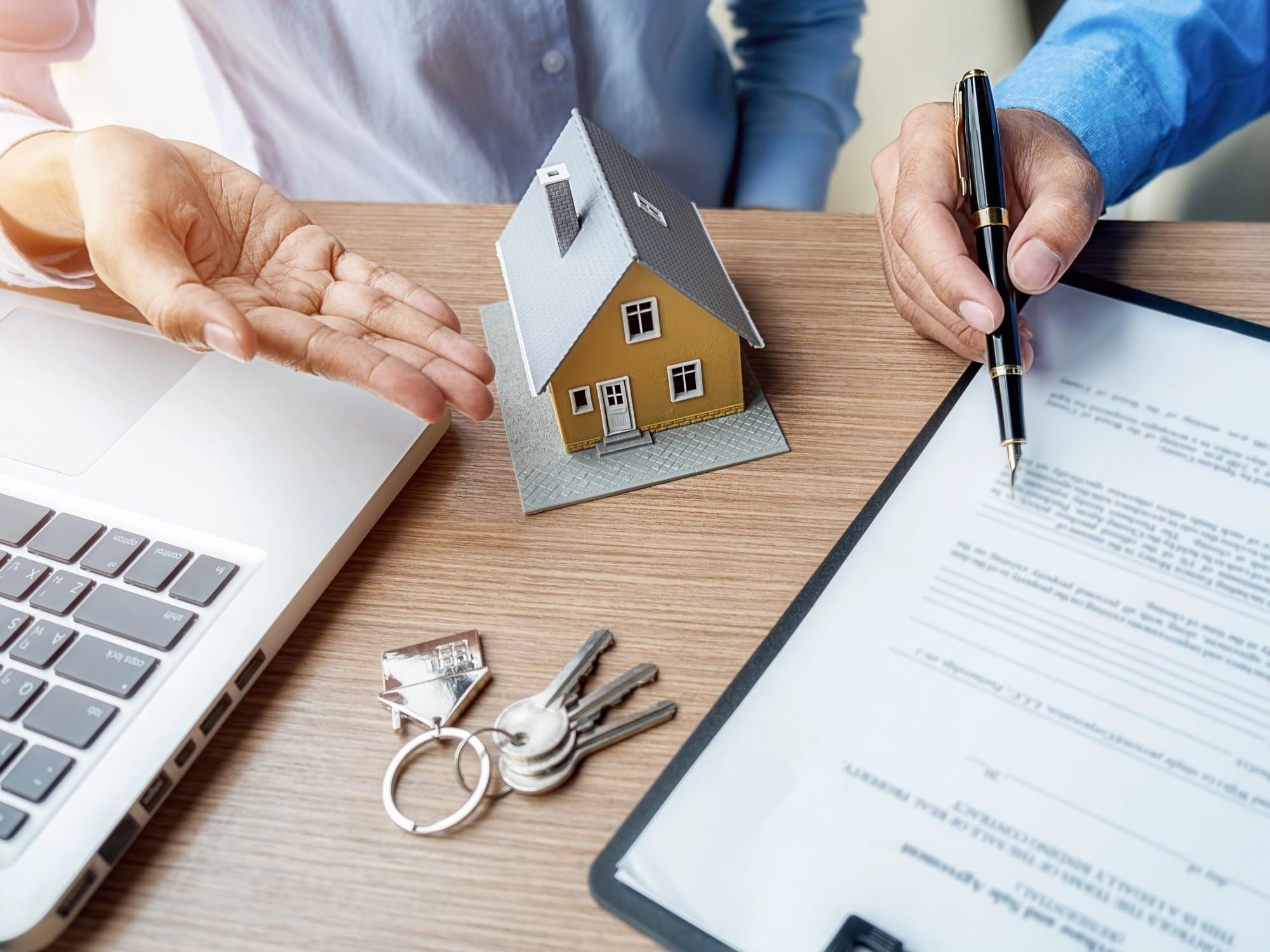 A buyer and seller at a desk with a model house, keys and a property transfer contract